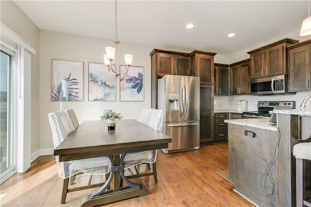 kitchen featuring light stone counters, stainless steel appliances, light hardwood / wood-style floors, and hanging light fixtures