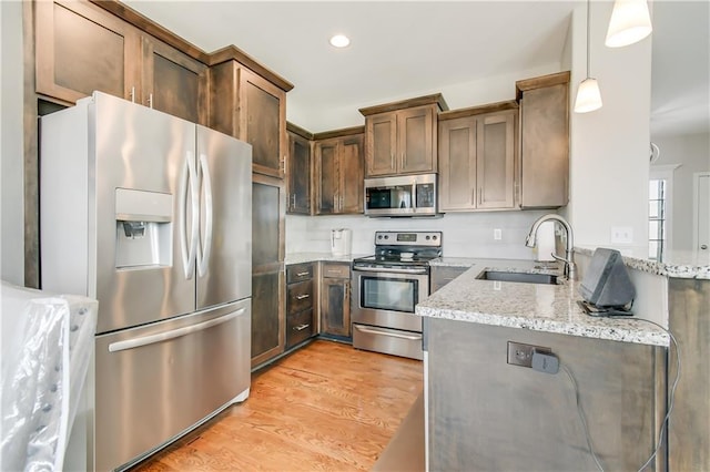 kitchen featuring appliances with stainless steel finishes, pendant lighting, sink, light stone counters, and light hardwood / wood-style floors