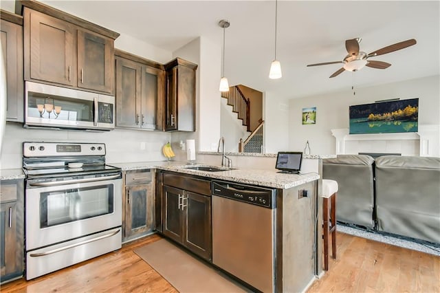 kitchen with decorative light fixtures, light stone counters, kitchen peninsula, stainless steel appliances, and dark brown cabinets