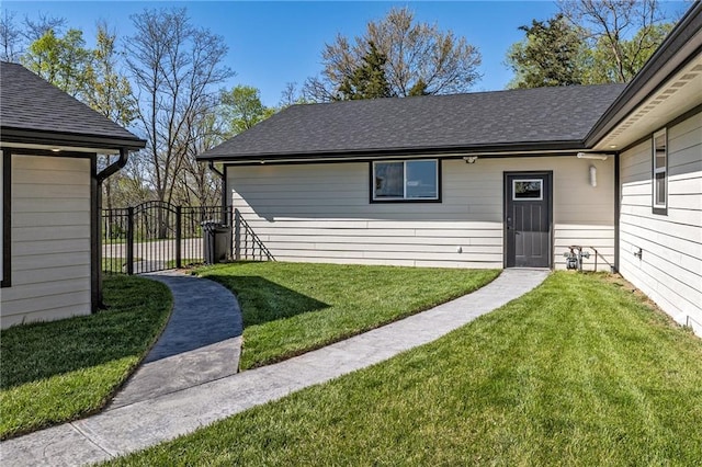 view of exterior entry featuring a gate, roof with shingles, fence, and a yard