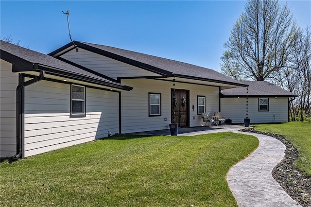 rear view of property with a patio area, roof with shingles, and a yard