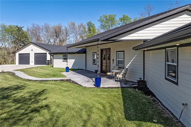 back of property with concrete driveway, an attached garage, a yard, and a patio