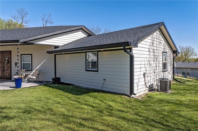 back of house featuring a shingled roof, a patio area, a lawn, and central AC unit