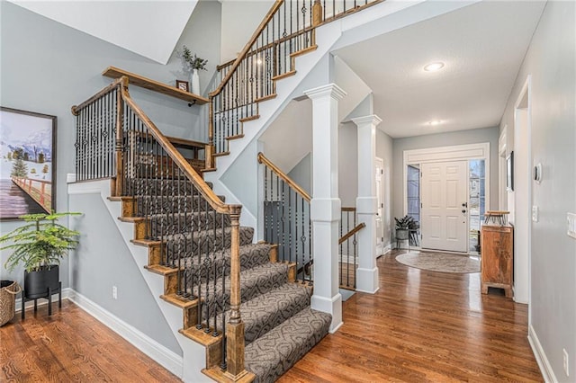 entryway featuring decorative columns, wood-type flooring, and a towering ceiling