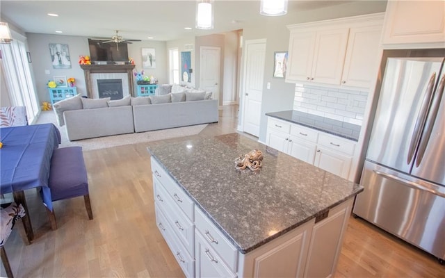 kitchen with a tile fireplace, white cabinetry, a kitchen island, and stainless steel fridge