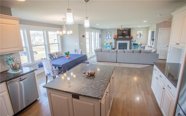 kitchen with decorative light fixtures, a center island, dark stone countertops, stainless steel dishwasher, and a fireplace