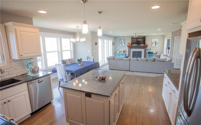 kitchen with a center island, hanging light fixtures, a tile fireplace, stainless steel appliances, and decorative backsplash