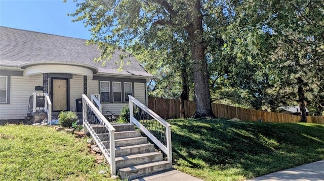 view of front facade featuring stairs, a front yard, fence, and a shingled roof