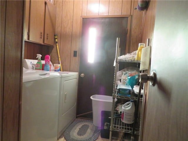 clothes washing area with cabinets, washing machine and clothes dryer, and wood walls