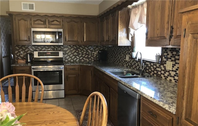 kitchen featuring sink, light tile patterned floors, appliances with stainless steel finishes, light stone counters, and decorative backsplash