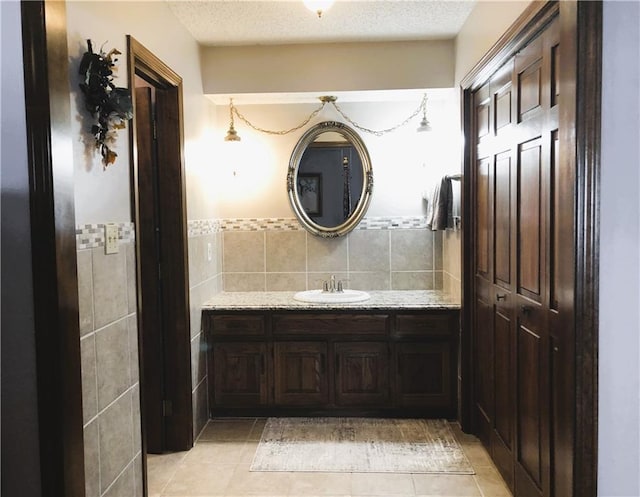 bathroom with vanity, tile patterned flooring, tile walls, and a textured ceiling