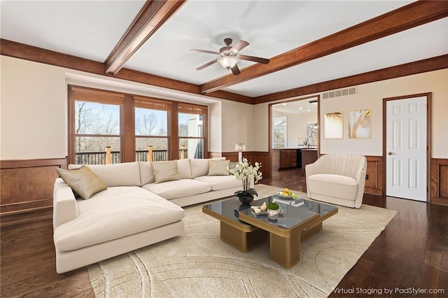 living room featuring beamed ceiling, a healthy amount of sunlight, and wainscoting