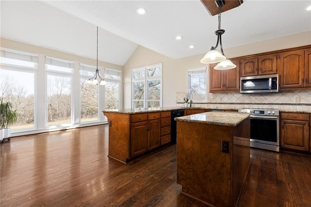 kitchen with light stone countertops, a kitchen island, vaulted ceiling, appliances with stainless steel finishes, and brown cabinets