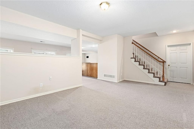 below grade area featuring stairs, visible vents, a textured ceiling, and carpet flooring