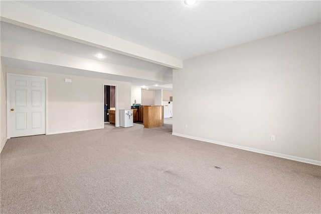 unfurnished living room featuring beamed ceiling, light colored carpet, and baseboards