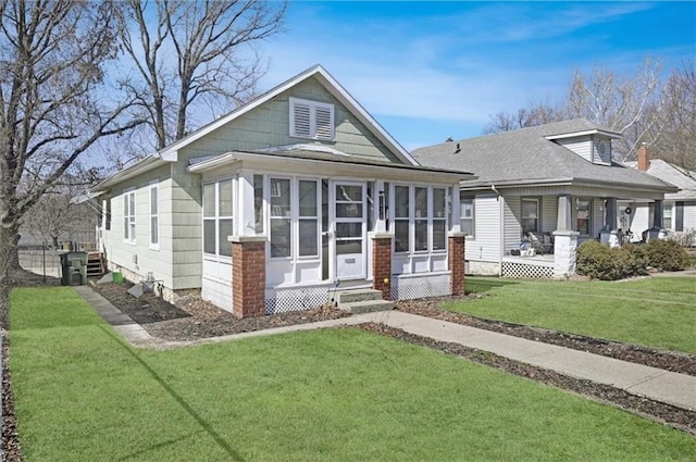 view of front facade featuring a shingled roof, a front yard, and a sunroom