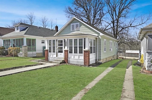 view of front of house featuring a shingled roof, a front yard, a sunroom, and fence