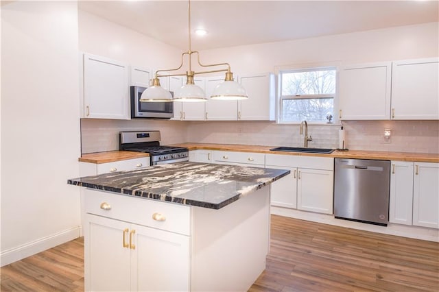 kitchen featuring sink, appliances with stainless steel finishes, white cabinets, a kitchen island, and decorative light fixtures