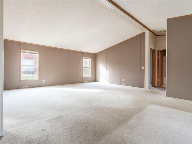 carpeted spare room featuring vaulted ceiling, ornamental molding, and a textured ceiling