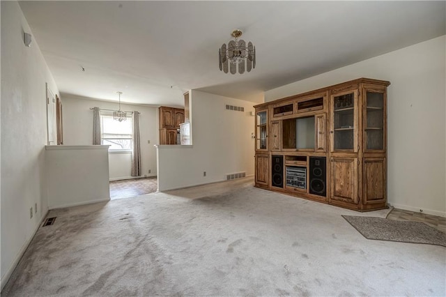 unfurnished living room featuring light carpet and an inviting chandelier