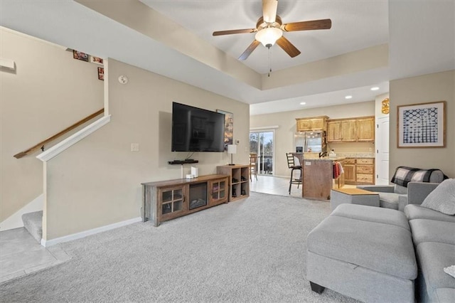 living room with a raised ceiling, light colored carpet, and ceiling fan