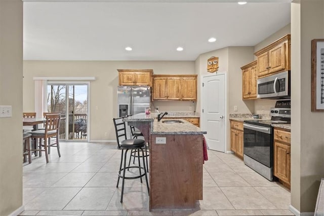 kitchen featuring sink, a center island with sink, stainless steel appliances, light stone counters, and a kitchen bar