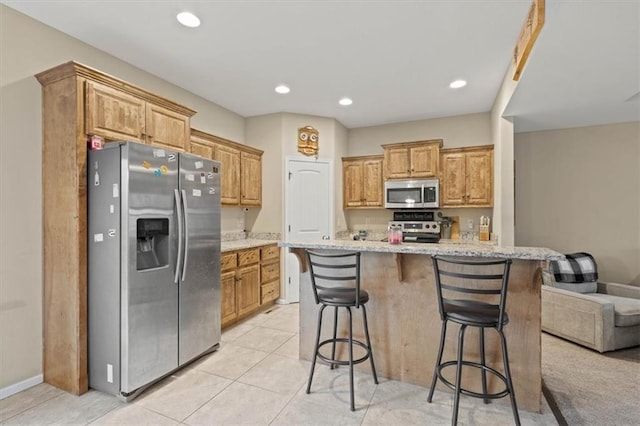 kitchen featuring light stone counters, stainless steel appliances, a kitchen breakfast bar, and a center island with sink