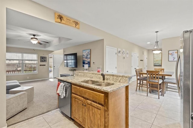 kitchen featuring sink, stainless steel appliances, light stone counters, a tray ceiling, and decorative light fixtures