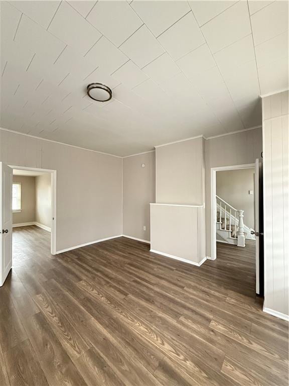 empty room with dark wood-style floors, crown molding, baseboards, and stairs