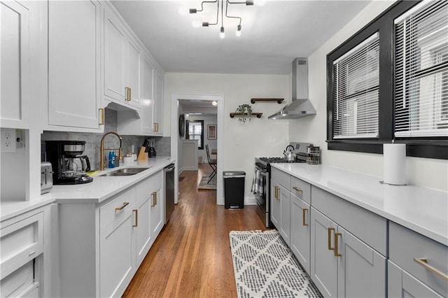 kitchen featuring sink, appliances with stainless steel finishes, tasteful backsplash, wall chimney exhaust hood, and light wood-type flooring