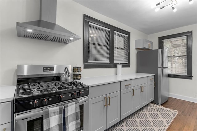 kitchen with wall chimney exhaust hood, stainless steel appliances, light hardwood / wood-style flooring, and gray cabinetry