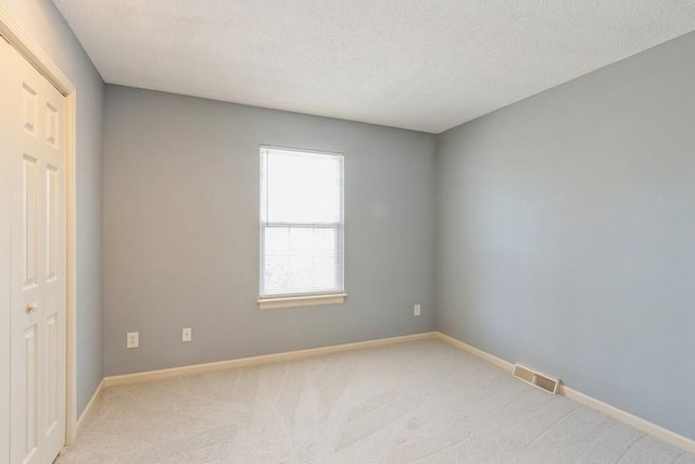 spare room featuring light carpet and a textured ceiling