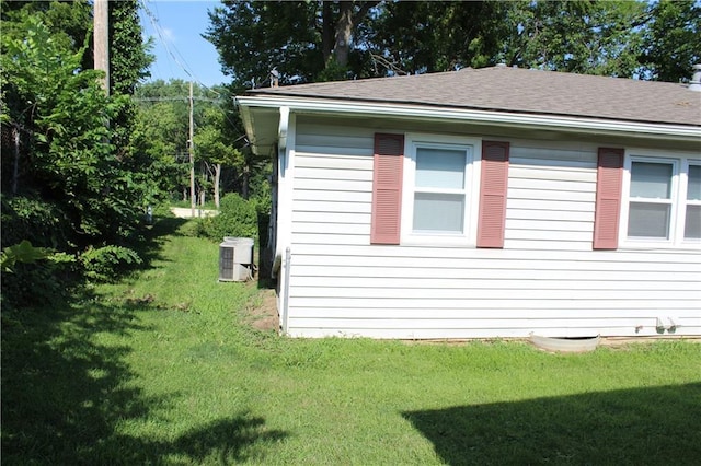 view of side of property featuring roof with shingles, central AC unit, and a yard