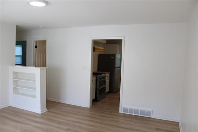 empty room featuring baseboards, light wood-style flooring, and visible vents