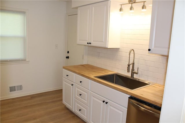 kitchen with stainless steel dishwasher, a sink, wood counters, visible vents, and white cabinets