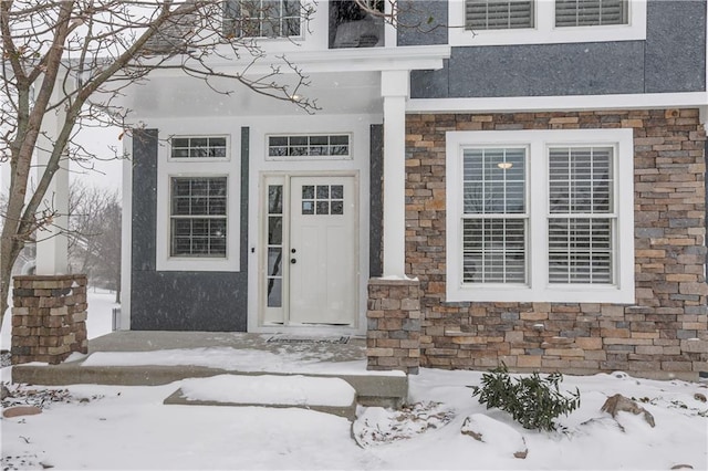 snow covered property entrance with stone siding and stucco siding