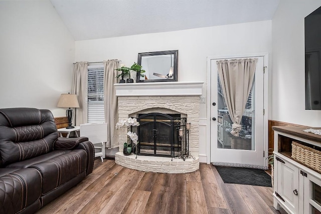 living room with hardwood / wood-style flooring, vaulted ceiling, and a stone fireplace