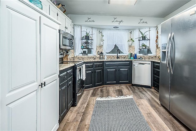 kitchen featuring hardwood / wood-style flooring, stainless steel appliances, sink, tasteful backsplash, and white cabinets