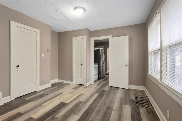 unfurnished bedroom with a textured ceiling, stainless steel fridge with ice dispenser, multiple windows, and light hardwood / wood-style flooring