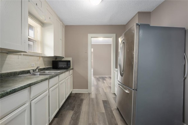 kitchen with sink, dark wood-type flooring, stainless steel refrigerator, white cabinetry, and a textured ceiling