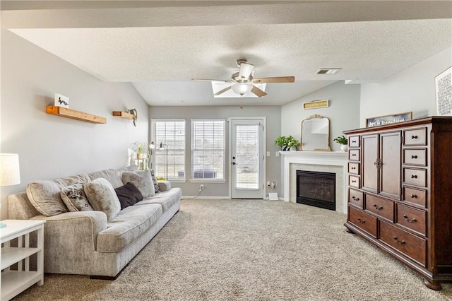 living area with lofted ceiling, a ceiling fan, a glass covered fireplace, light carpet, and a textured ceiling