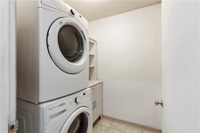 washroom featuring stacked washer / drying machine, cabinet space, and baseboards