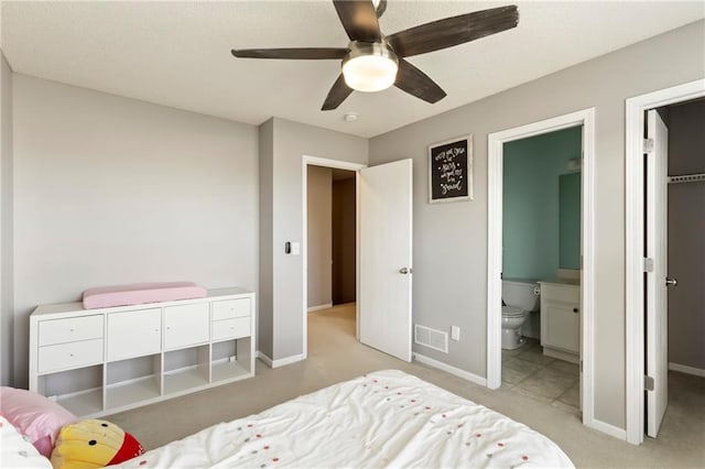 bedroom featuring light colored carpet, a ceiling fan, visible vents, baseboards, and ensuite bath