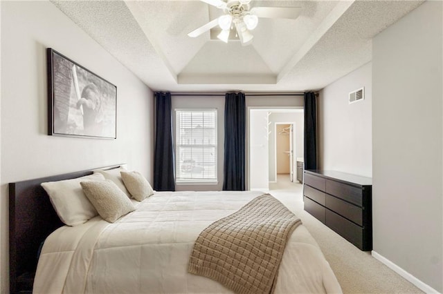 carpeted bedroom with a ceiling fan, a textured ceiling, visible vents, and a tray ceiling