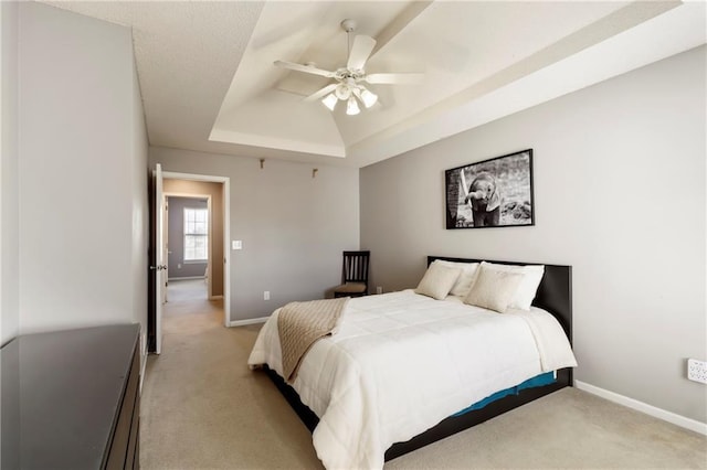 bedroom featuring light carpet, baseboards, a tray ceiling, and ceiling fan