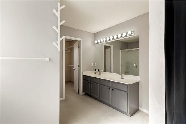 bathroom featuring double vanity, a spacious closet, a sink, and baseboards