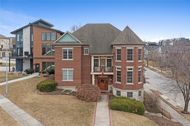 townhome / multi-family property with roof with shingles, brick siding, a balcony, and a front lawn