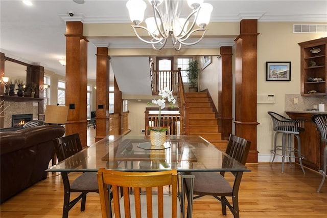 dining space with decorative columns, visible vents, light wood-style flooring, stairs, and a chandelier