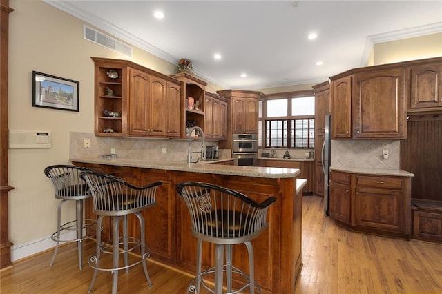 kitchen with open shelves, visible vents, light wood-style floors, a sink, and a peninsula