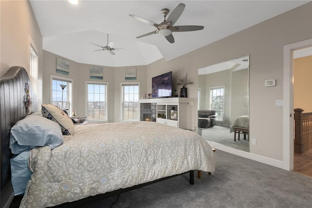 carpeted bedroom featuring vaulted ceiling, ceiling fan, a tiled fireplace, and baseboards